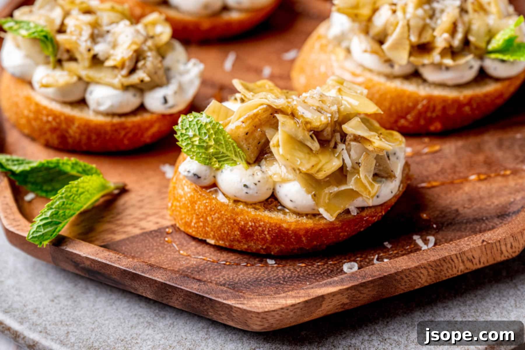 A top-down view of a plate of Marinated Artichoke Hearts Crostini, with a wine glass in the background.